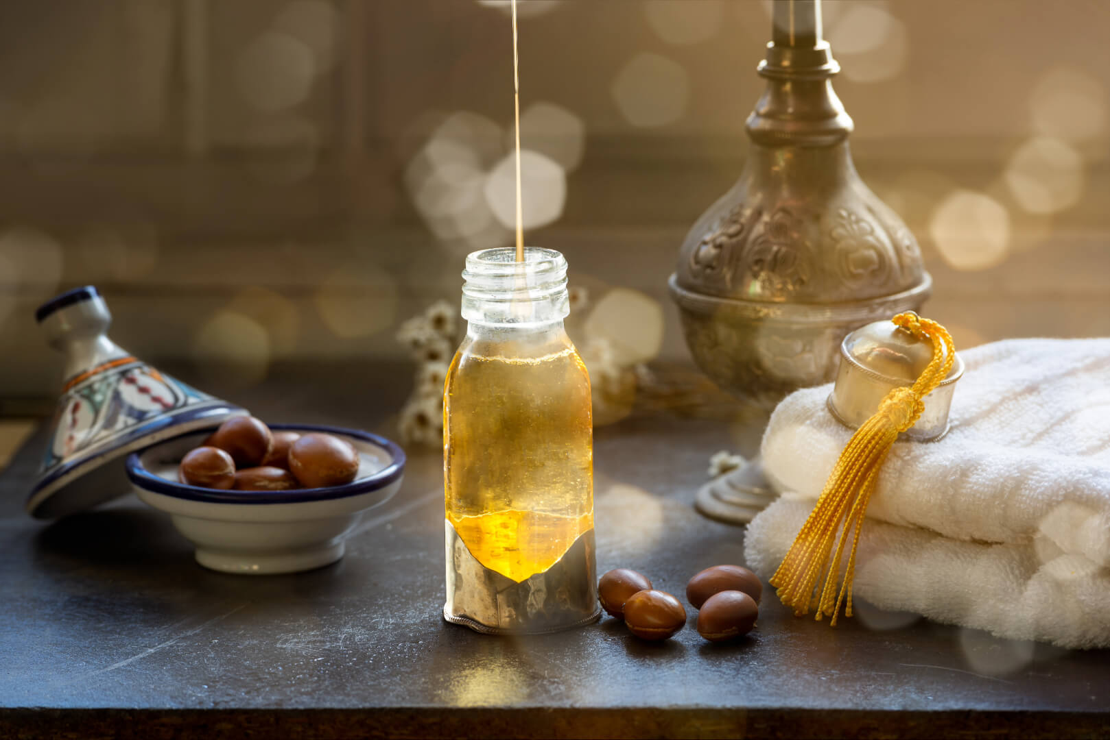 Bouteille en verre dans un décor marocain contenant de l'huile d'argan avec des fruits de l'arganier autour