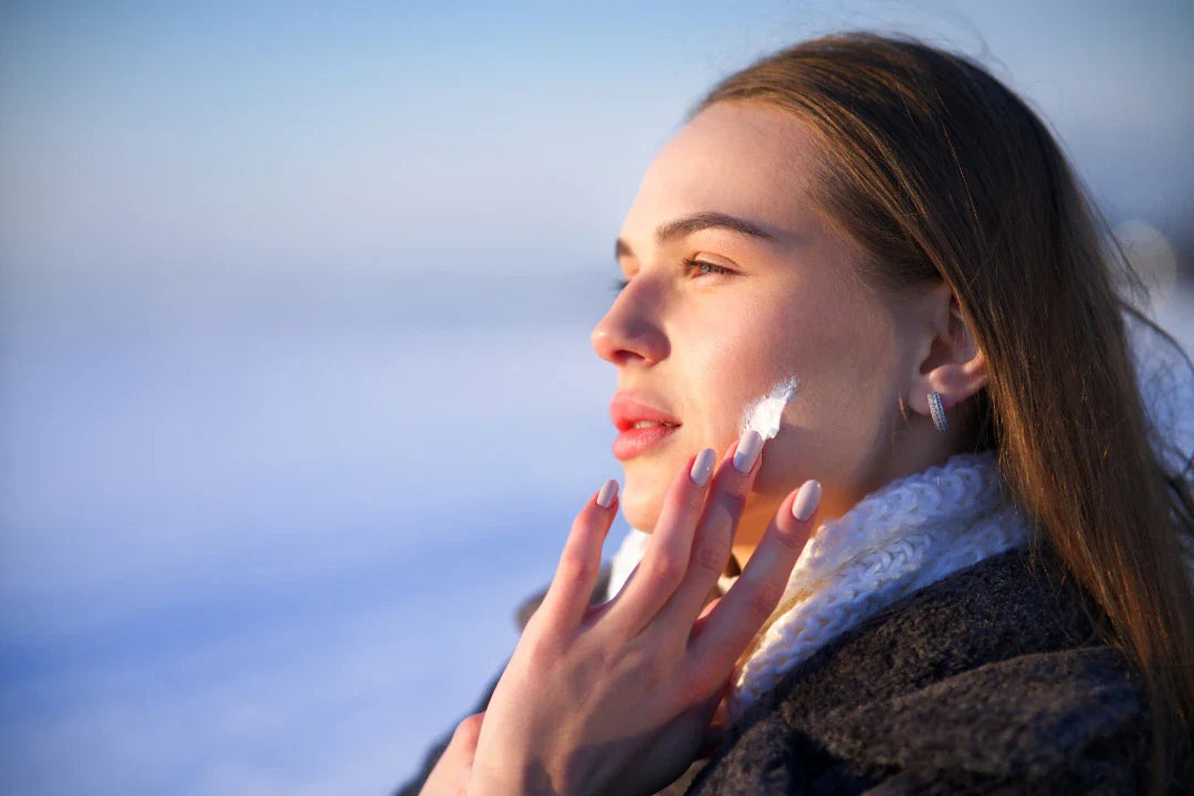 Portrait d'une belle femme appliquant une crème hydratante oriental treasure pour la peau sur le visage et les mains, se protégeant du froid en hiver. Jolie fille prend soin de sa peau à l'extérieur sur fond de nature enneigée.