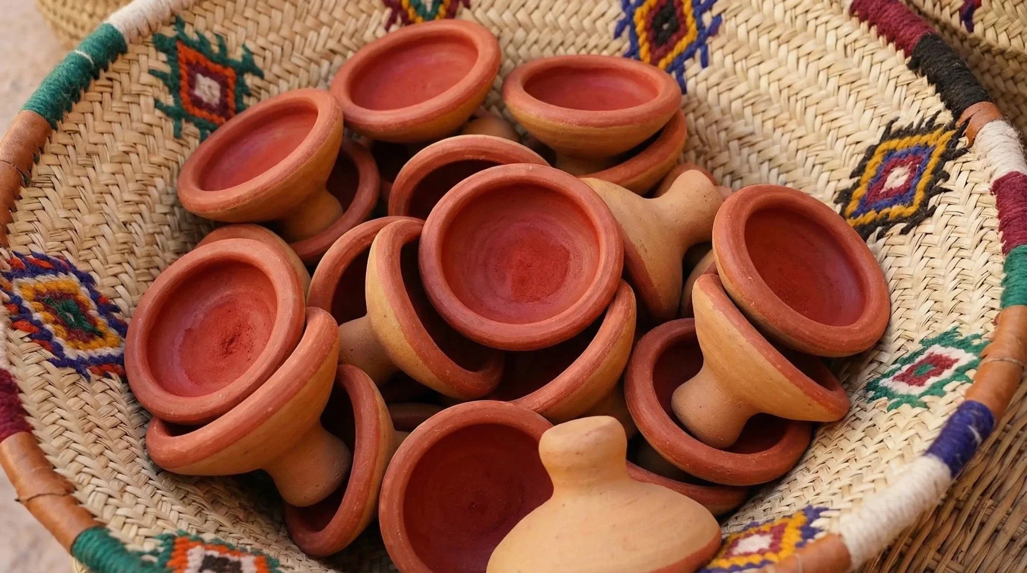 Petits dômes en terre cuite garnis de pigment rouge aker fassi, dans un panier tressé berbère