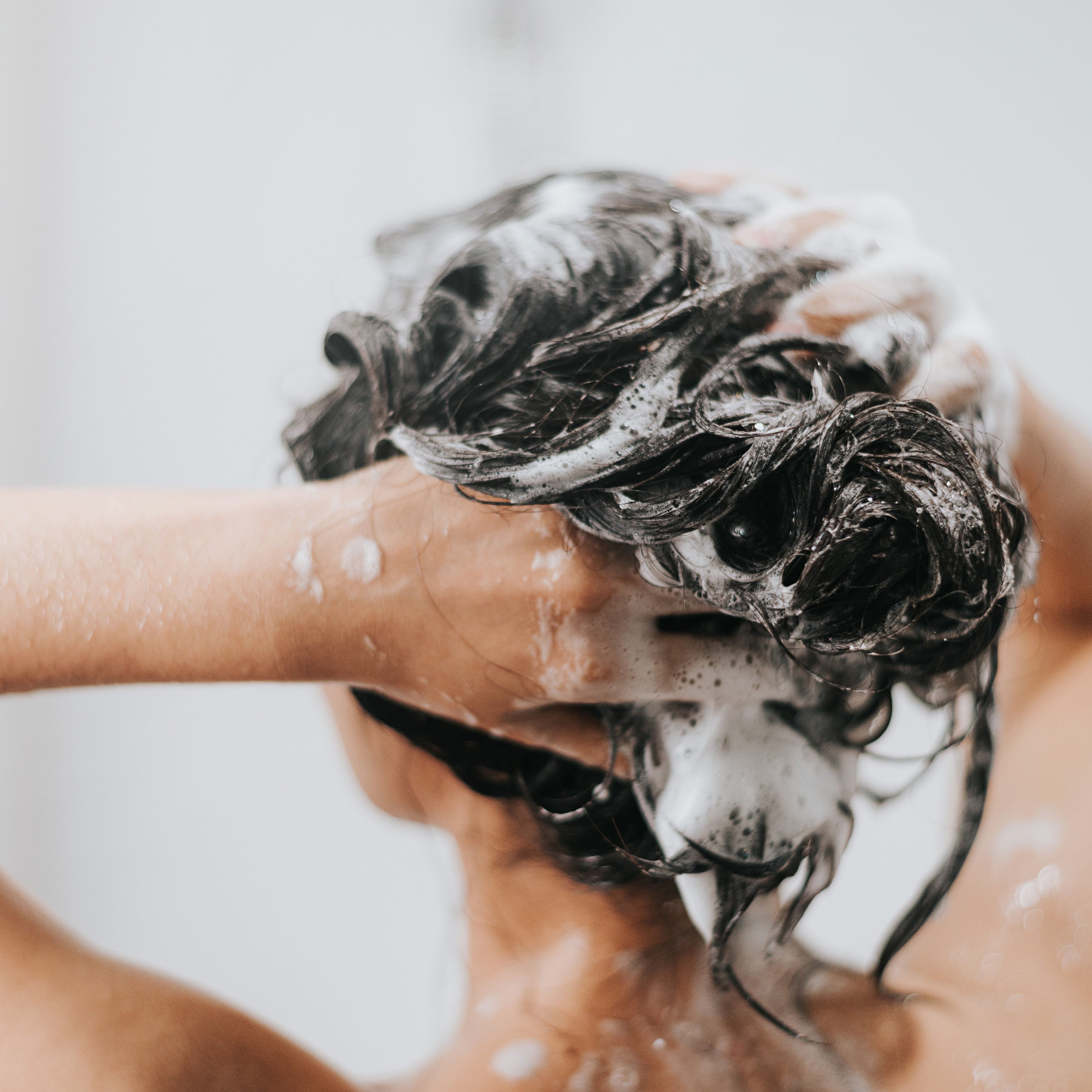 Femme se lavant les cheveux avec du shampoing sous la douche , soins capillaires avec de la mousse pour la fraîcheur. Spa et soins de santé.