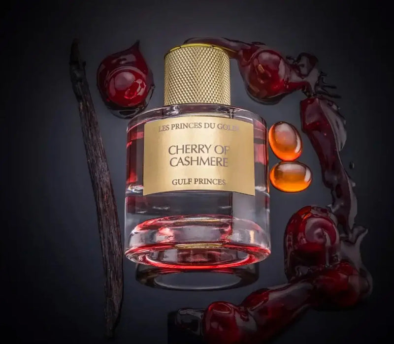 Sur fond noir flacon de parfum cherry of cashmere de la marque les princes du golfe entouré de cerise, de gousse de vanille et de morceaux de mandarine