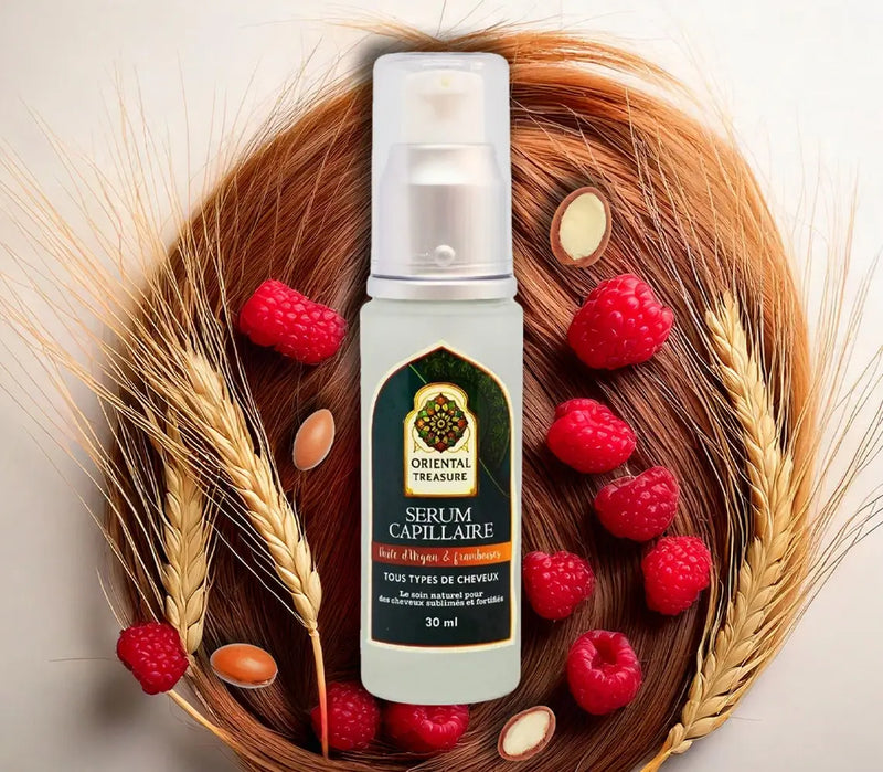 Flacon de sérum capillaire à base d'huile d'argan et framboise posé sur des cheveux et entouré d'épis de blé de framboise et des fruits d'arganier